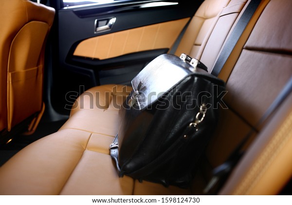 business\
leather briefcase on backset of luxury\
car
