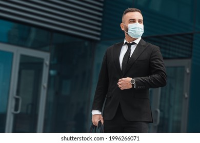 Business life. Mature businessman in face mask adjusting suit button, elegnat handsome man standing outdoors against business center. Successful executive in fashionable formal suit - Powered by Shutterstock