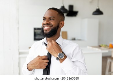 Business Lifestyle Concept. Portrait Of Smiling Confident Young African American Businessman Adjusting Necktie At Home, Getting Ready For Work, Wearing White Shirt And Luxury Watch