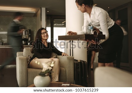 Business lounge staff serving coffee to female traveler at waiting area. Business woman waiting at airport departure lounge.