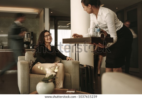 Business lounge staff serving coffee to female\
traveler at waiting area. Business woman waiting at airport\
departure lounge.