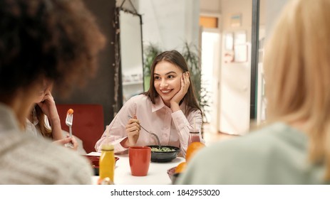 Business lunch. A fashionably dressed young brown haired woman smiling and sitting at a table with her female collaborateurs during a business lunch in a well-lighted creative office - Powered by Shutterstock