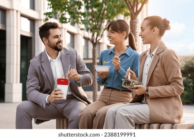 Business lunch. Happy colleagues spending time together during break on bench outdoors - Powered by Shutterstock