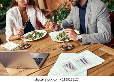 Business lunch. Man and woman sitting at table at restaurant eating healthy fresh salad discussing project close-up