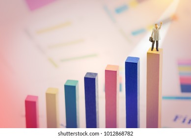 Business magnate or powerful personal business ownership concept : Miniature figurine businessman in a grey overcoat carries a briefcase, raises his left hand, stands on the first place wood pole. - Shutterstock ID 1012868782