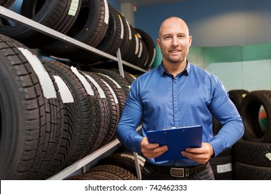 Business, Maintenance And People Concept - Male Manager With Wheel Tires And Clipboard At Car Repair Service Or Auto Store