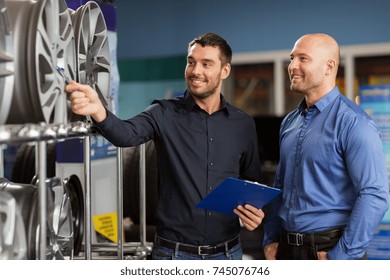 business, maintenance and people concept - male customer and salesman with clipboard showing alloy wheel rims at car repair service or auto store