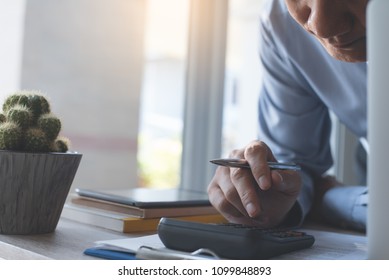 Business man, accountant holding pen and using calculator to calculate financial report, working laptop computer on desk at home office, close up, front view. Business and finance concept
