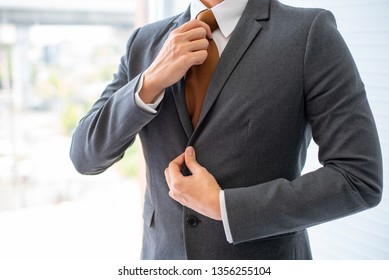 Business man with the action of dressed up his necktie and grey suit in front of glass window in the office. Concept of good management in business system to get better opportunity of successful. - Powered by Shutterstock