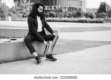 Business Man Adjusting His Prosthetic Leg Outdoor From Office Building - Focus On Hands Holding Prosthesis - Black And White Editing