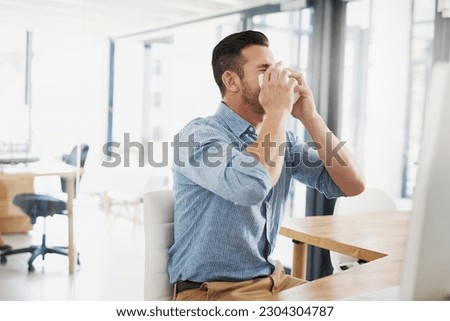 Business man, blowing nose and allergy in office with flu, virus and tissues for healthcare at desk. Young businessman, allergies or sick with hayfever, toilet paper and cleaning mucus in workplace