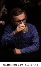 Business man, in blue shirt and glasses, drinking cocktail of vintage old fashion glass in loft bar