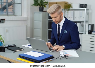 Business Man In Blue Suit Typing On Computer On Desk In Office. Eyeglasses And Reports On Surface.