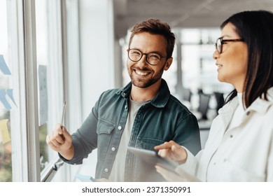 Business man brainstorming with his colleague using sticky notes. Creative business people standing next to a window and discussing their ideas. - Powered by Shutterstock