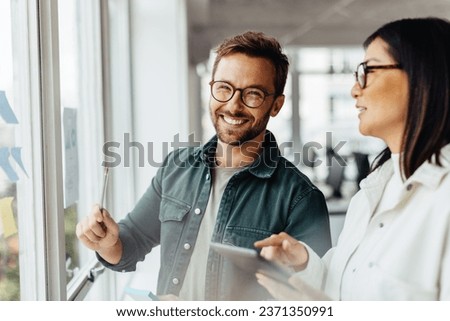 Business man brainstorming with his colleague using sticky notes. Creative business people standing next to a window and discussing their ideas.