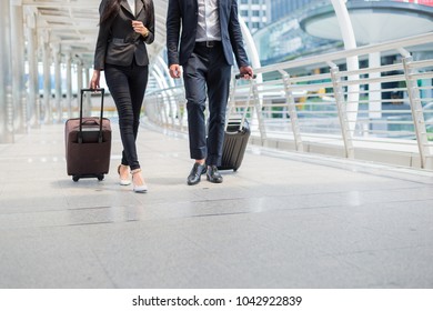 Business Man And Businesswoman Wear Black Suit Walk Together With Luggage On The Public Street, Business Travel Concept