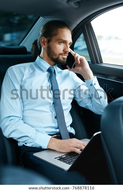 Business Man In Car Calling On\
Phone While Going To Work. Handsome Smiling Young Male Talking On\
Smartphone, Sitting On Back Seat Of Business Car. High Quality\
Image.