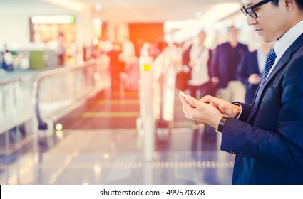 Business Man Is Doing Business On Mobile Phone, While Is Sitting In Airport Near Window With Sun Rays During His Business Trip.