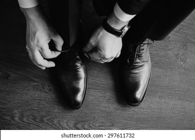 Business man dressing up with classic, elegant shoes. Groom wearing shoes on wedding day, tying the laces and preparing. Black and white photo