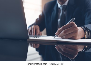 Business man, executive manager hand with a pen writing on notepad, working in modern office with laptop computer and digital tablet on desk, project planning, work process concept, close up