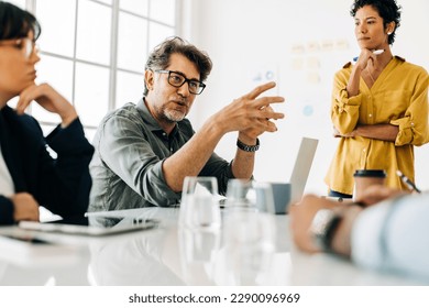 Business man explaining a project to his team. Senior business man taking the lead during a meeting. Group of business people discuss about work in an office.