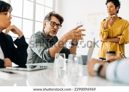 Business man explaining a project to his team. Senior business man taking the lead during a meeting. Group of business people discuss about work in an office. [[stock_photo]] © 