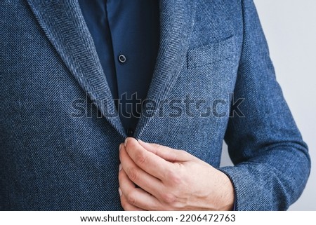 Business man fastens a button on blue tweed blazer with dark blue shirt, hands close-up.