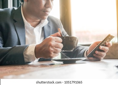 Business Man, Freelancer Using Mobile Smart Phone, Drinking Coffee, Working On Laptop Computer Near The Window At Home Office With Morning Sunlight.