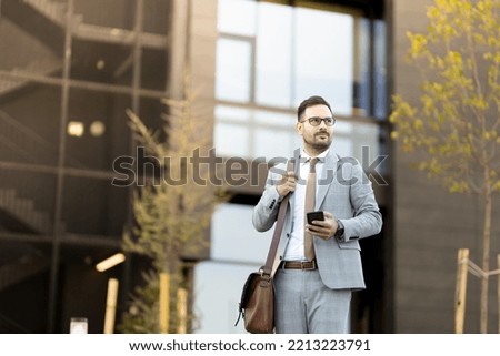 Business man in front of modern office building Warm light coloured Business man walking of his office and looking on phone