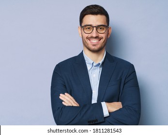 Business Man In Glasses And Formal Clothes Looking At Viewer With Confidence And Friendly Smile, Standing With Arms Crossed, Isolated On Blue Background, Copy Space On Left