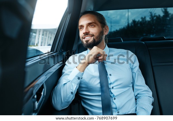 Business Man Going To Work In Car. Portrait Of
Handsome Successful Young Businessman In Formal Wear Traveling On
Back Seat Of Vehicle And Looking Through Window. Business Travel.
High Quality Image.