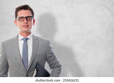 Business man with grey suit. He is holding a black folder. Over concrete wallpaper