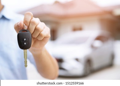 Business Man Hand Holding Car Keys Front With New Car On Background. Parking In Front Of The House. Transportation Concept. Leave Copy Space To Write Messages Text.