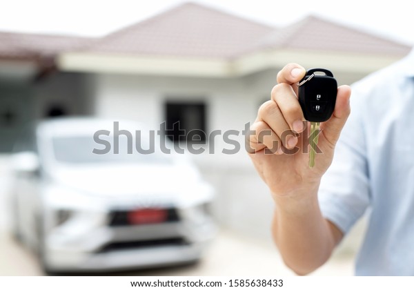 Business man hand holding car keys\
front with new car on background. parking in front of the house.\
transportation concept. Leave copy space to write messages\
text.