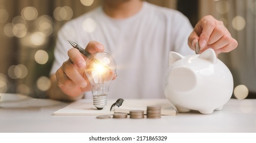 business man hand holding lightbulb and putting coin in to the piggy bank. idea saving energy and accounting finance in home and family concept, save world and energy power. - Shutterstock ID 2171865329