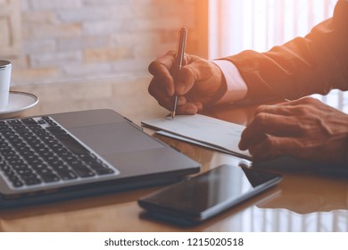 Business Man Hand Holding Pen, Writing And Signing Checkbook , Work On Laptop Computer With Mobile Smart Phone On The Desk At Modern Office. Payment By Cheque Concept.