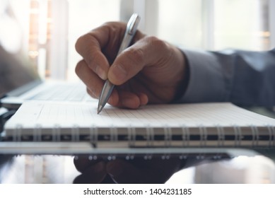 Business man hand write his work plan on paper notebook with a pen while working in modern office. Man student taking note while learning online course via laptop computer, close up, elearning concept - Shutterstock ID 1404231185
