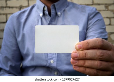 Business Man Handing A Blank Business Card Over Background White Brick Wall On The Street. A Plastic Credit Card Or Business Card As A Mockup For Design Or Text With An Empty Space.