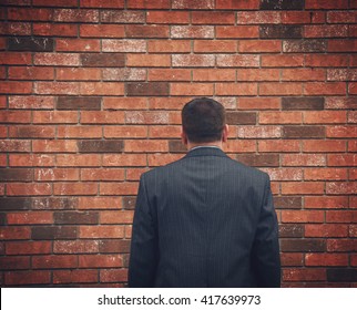 A business man has his back turned and looking at a brick wall. Can represent an obstacle, sadness or a struggle. - Shutterstock ID 417639973