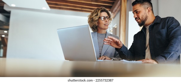 Business man having a discussion with his colleague in an office. Two business people using a laptop in a meeting. Teamwork and collaboration between business professionals. - Shutterstock ID 2255732387