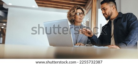 Business man having a discussion with his colleague in an office. Two business people using a laptop in a meeting. Teamwork and collaboration between business professionals.