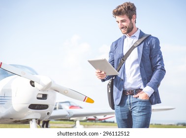 Business Man With His Airplanes. He Is Walking In The Airport With The Tablet Checking The Schedule.