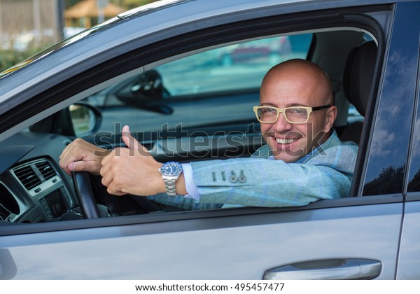 Business man  in his car smiling, showing thumbs\
up, like happy with his car\
choice