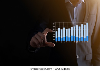 Business man holding holographic graphs and stock market statistics gain profits. Concept of growth planning and business strategy. Display of good economy form digital screen - Shutterstock ID 1905431656