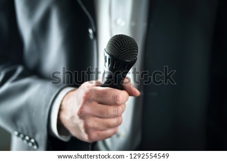 Business man holding microphone. Public speaking and giving speech in suit for audience concept. Fiance, host or best man giving toast with mic in wedding. Karaoke, talent show or singing contest.
