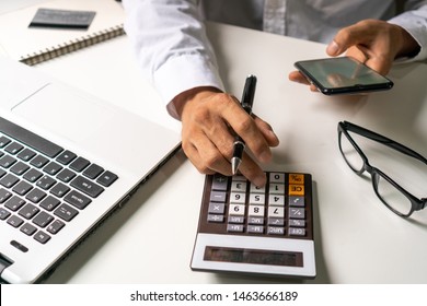 A Business Man Holding Pen While Using Calculator And Smartphone In His Office, Business Work Concept.