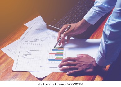 Business Man Holding Pen And Writing Note On The Wood Table,Checklist Note Financial Leverage Investment Data, Home Office Desk Background Textures Concept.