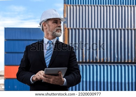 Business man holding a tablet  and checking the list of export and import orders through the port stands at the container yard. Serious boss  working and confront and solve a problem at logistic cargo