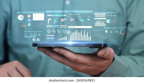 Business man holding tablet with a projected digital interface showing business analytics, charts, and data dashboards. Futuristic technology and digital transformation.
