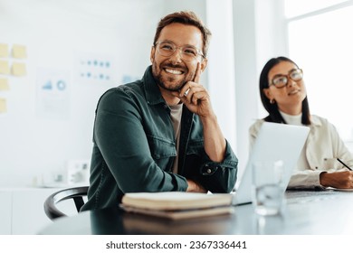 Business man listening to a discussion during a meeting in an office. Happy business man sitting in a boardroom with his colleagues. - Shutterstock ID 2367336441